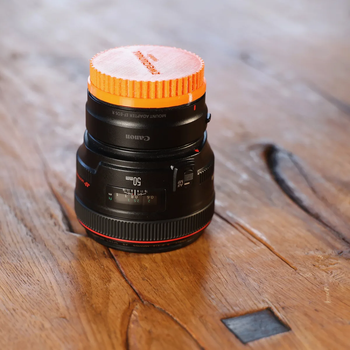 Canon EF 50 mm f/1.2 L mit EF-EOS-R-Adapter, stehend mit orangefarbener Frontkappe