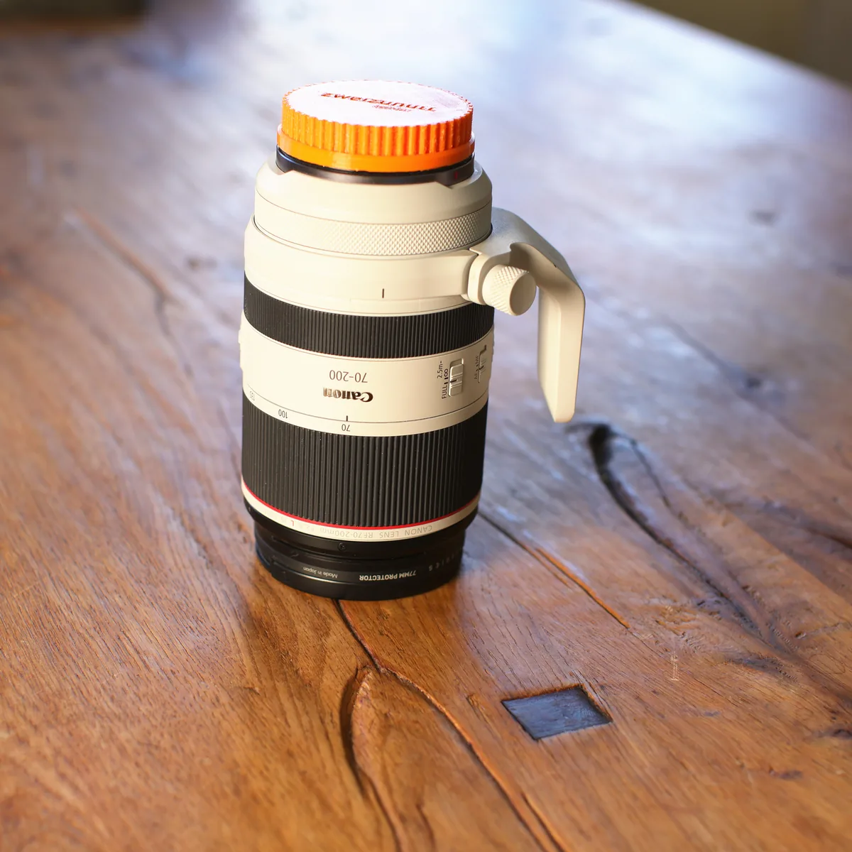 Canon RF 70-200 mm f/2.8 L in Weiß, stehend mit Stativschelle und orangefarbener Frontkappe